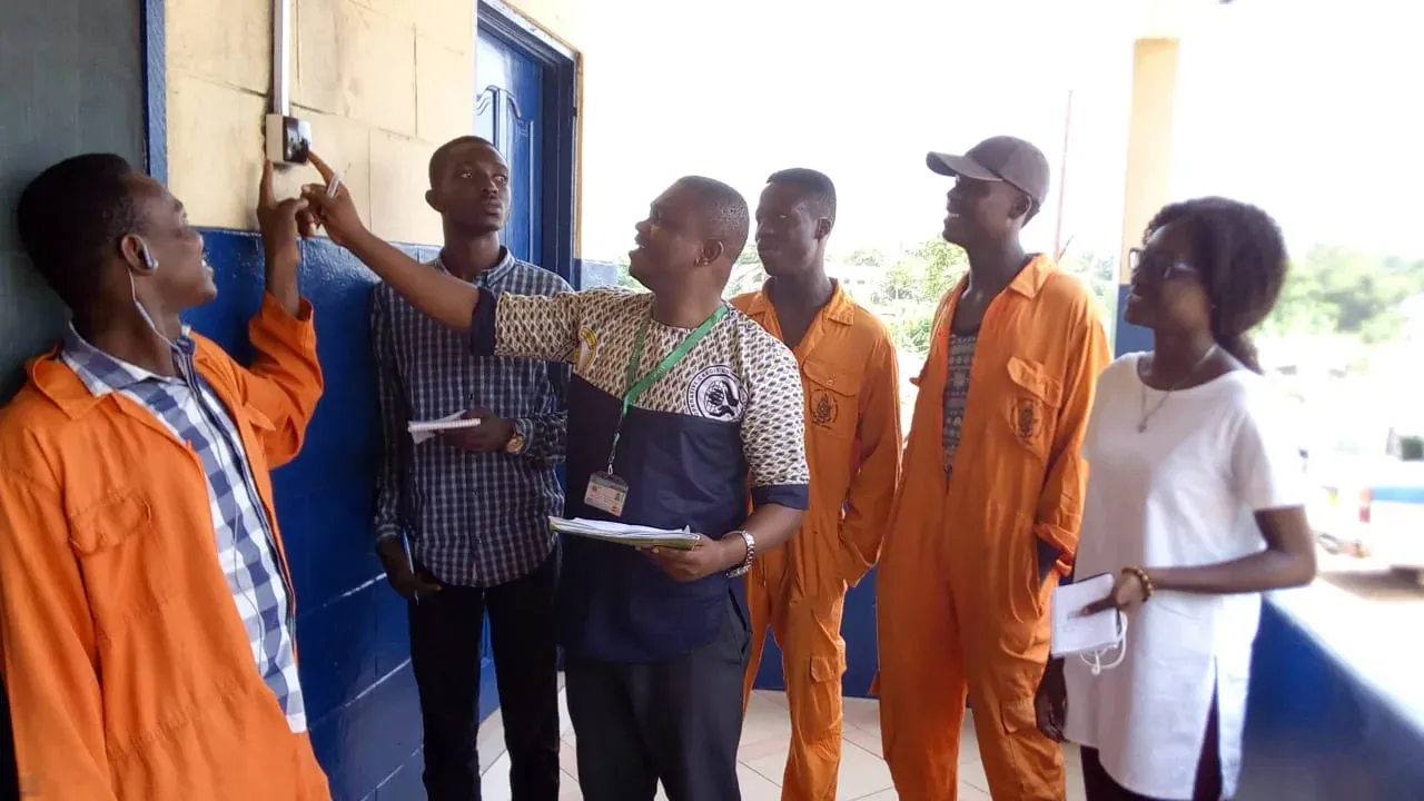 Instructor showing trainees in overalls a wall-mounted meter installation