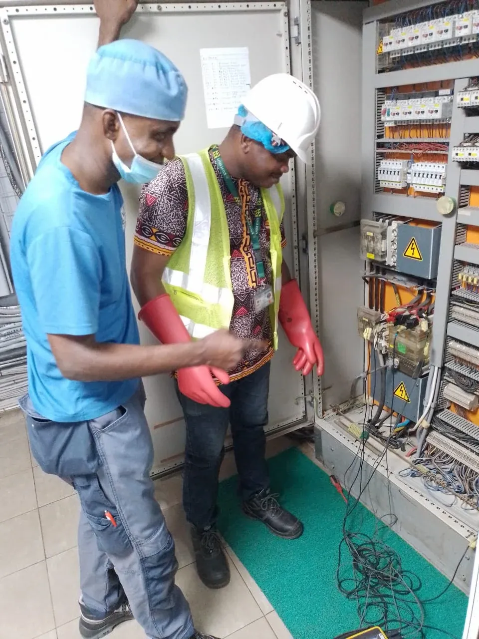 Two engineers inspecting an industrial control panel, one wearing insulated gloves