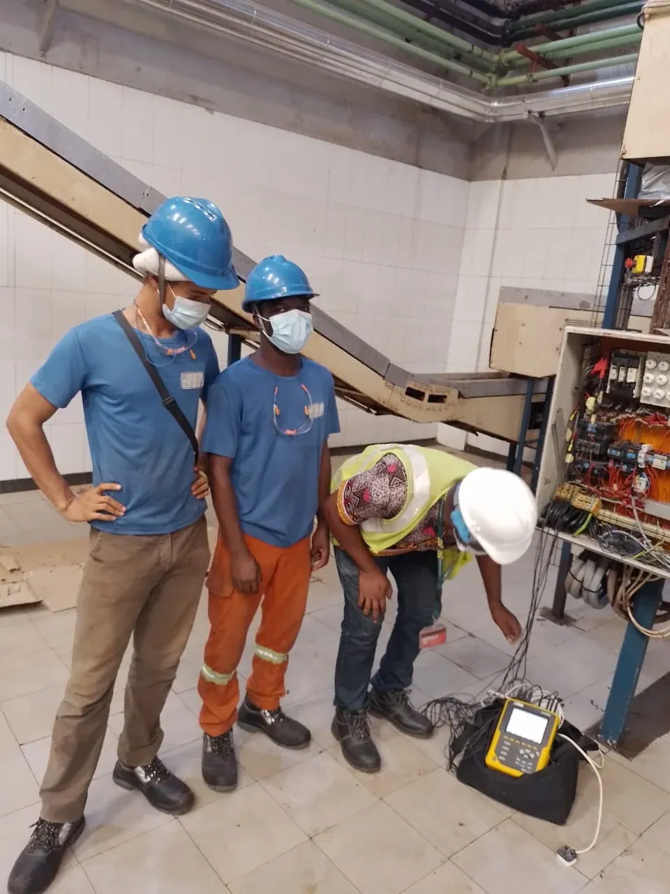 Engineer connecting a power quality analyser to a motor control panel while technicians observe